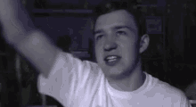 a man in a white t-shirt is raising his arm in the air .
