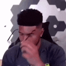 a man is sitting in a chair covering his nose with his hand while wearing glasses .