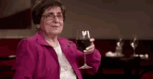a woman in a pink jacket is holding a glass of red wine .