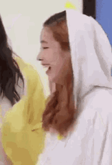 a woman in a white hoodie is laughing while standing next to another woman .