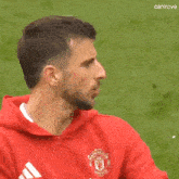 a man wearing a red manchester united hoodie is standing on a field .