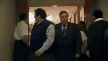 a man in a suit and tie is walking down a hallway with a group of people .