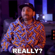 a man wearing a colorful hoodie and a hat is sitting in a chair and says really ?