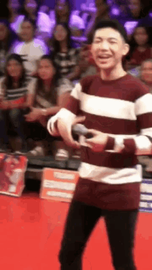 a man in a maroon and white striped sweater is standing on a red carpet holding a microphone .