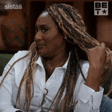a woman in a white shirt is holding her braided hair in front of a sign that says sistas