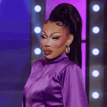 a woman wearing a purple jacket and hoop earrings looks at the camera