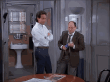 a man in a suit and tie is standing next to another man in a bathroom .