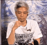 a man wearing a white t-shirt with a dragon on it is sitting in front of a painting .