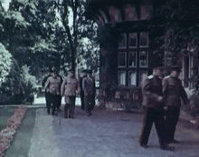 a group of men walking down a sidewalk with a building in the background
