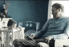 a man is sitting in a chair looking at a tablet while a baby is in a crib .