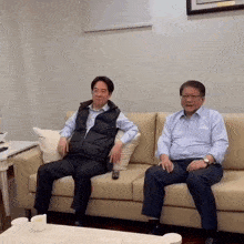 two men are sitting on a couch with a remote control .