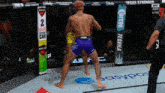 a fighter in purple shorts stands in front of a sign that says shots in every can