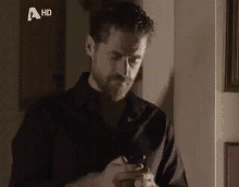 a man in a black shirt is using a cell phone with a hd logo behind him .