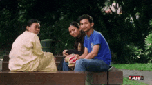 a man in a blue shirt sits on a wooden bench with two women