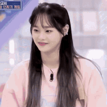 a girl with long hair and earrings is wearing a pink shirt and looking at the camera .