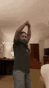 a man with a beard is stretching his arms in a living room with a viggle ai icon