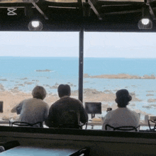 three people sit in front of a window overlooking the ocean with the letter x on the ceiling