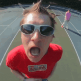 a man wearing sunglasses and a red t-shirt with a sticker on it that says ' a '