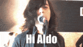 a man with long hair singing into a microphone with the words hi aldo below him