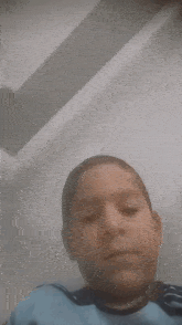 a young boy in a blue shirt is making a funny face while looking at the camera .