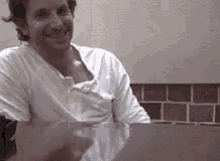 a man in a white shirt is sitting at a table with a laptop .