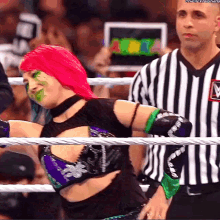 a woman with pink hair and green paint on her face stands in a wrestling ring