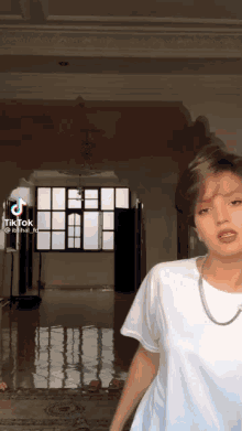 a woman in a white t-shirt is standing in front of a window in a room .