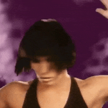 a woman with short black hair is standing in front of a purple background .
