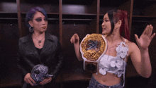 two women in a locker room one wearing a wrestling belt
