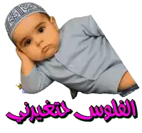 a baby wearing a hat and a blue shirt is laying down with arabic writing behind him