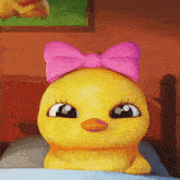 a yellow duck with a pink bow on its head laying on a bed