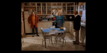 three people standing in a kitchen with a bottle of wine on a table
