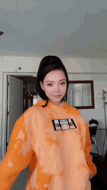 a woman wearing an orange tie dye hoodie with a picture of naruto on it