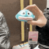 a person is holding a blue stuffed animal with a tag that says sanrio