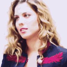 a woman with blonde hair wearing a blue jacket with red feathers on the collar