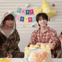 a man in a plaid shirt is sitting at a table with a cake and balloons .