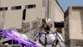 a purple sword is being held by a man in a silver suit with the letter b on his chest