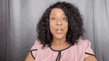 a woman with curly hair and a pink shirt is making a funny face .