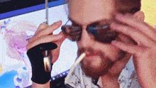 a man wearing sunglasses is smoking a cigarette in front of a computer screen