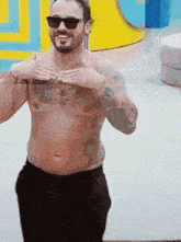 a shirtless man with a beard wearing sunglasses holds his hands to his chest