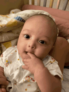 a baby wearing a white shirt with a bear on it biting his finger