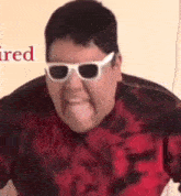 a man wearing sunglasses and a red shirt is sticking out his tongue .