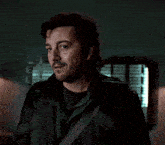 a man with a beard is wearing a green jacket and black shirt
