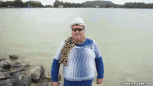 a man wearing sunglasses and a scarf is standing in front of a body of water ..