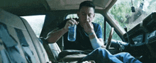 a man is sitting in the back seat of a car eating a sandwich and drinking water .