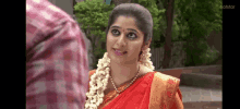 a woman in a red saree is standing next to a man in a plaid shirt .
