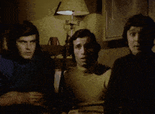 three men are sitting in front of a lamp that has the letter g on it