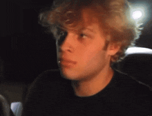 a man with curly hair is wearing a black shirt and looking at the camera .