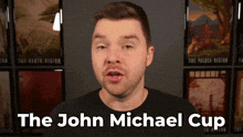 a man in a black shirt stands in front of a wall with pictures and the words " the john michael cup " above him