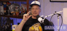 a man wearing a hat with the letter s on it is talking into a microphone in front of a shelf full of toys